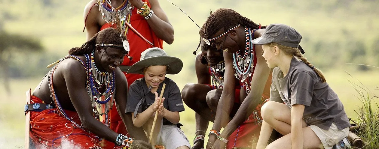 Maasai guides sitting with travellers on the grass, demonstrating fire-making
